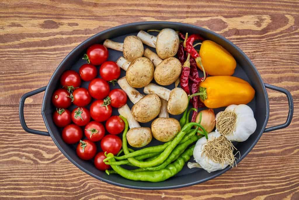 Cast iron dish filled with uncooked healthy vegetables including tomatoes, mushrooms and peppers