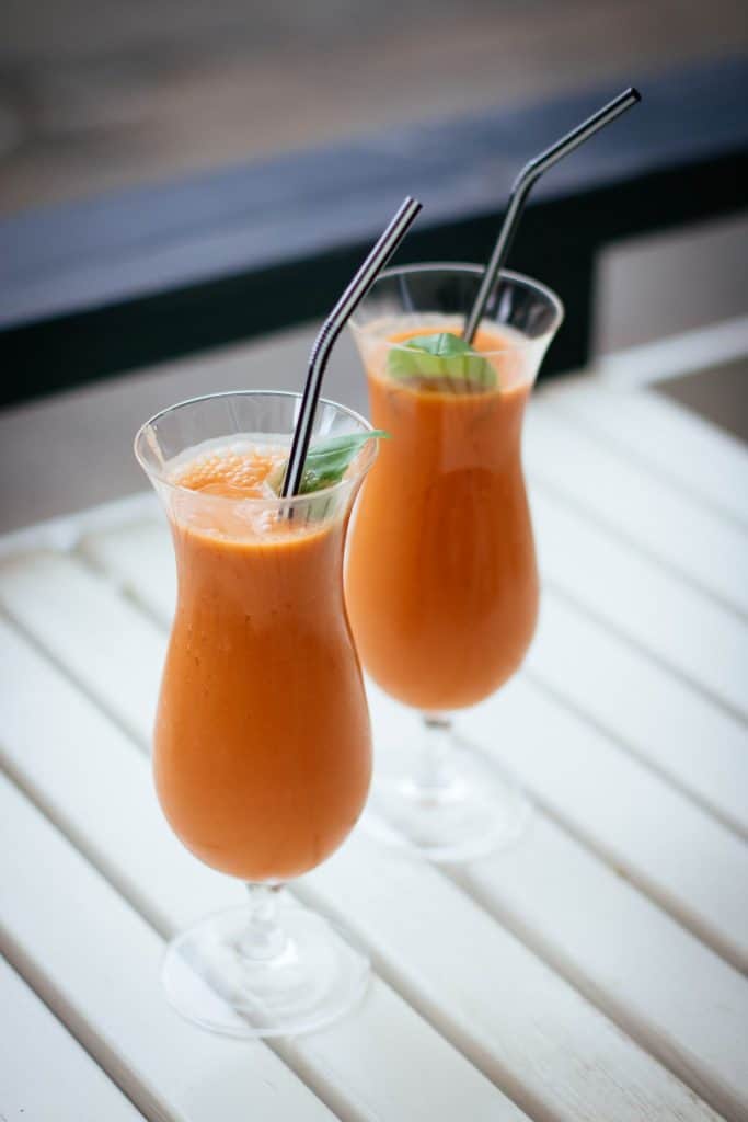 Two tall curved glasses of orange smoothie topped with mint leaf