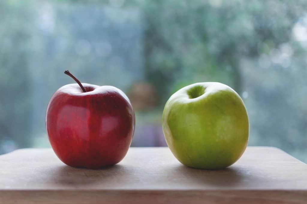 One red and one green apple side by side on a chopping board with a blurred out background